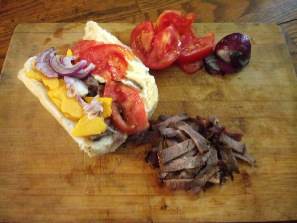 Dry Aged Chuck Steak On a Hoagie with American Cheese Red Onions and Tomatos.
