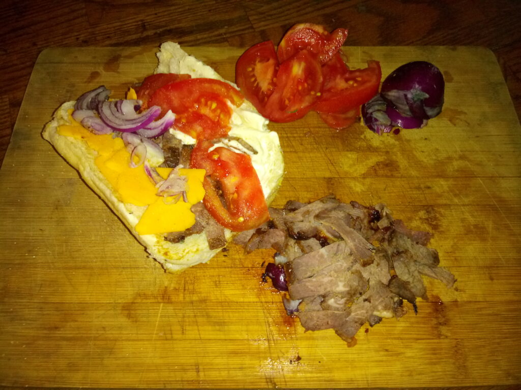Dry Aged Chuck Steak On a Hoagie with American Cheese Red Onions and Tomatos.